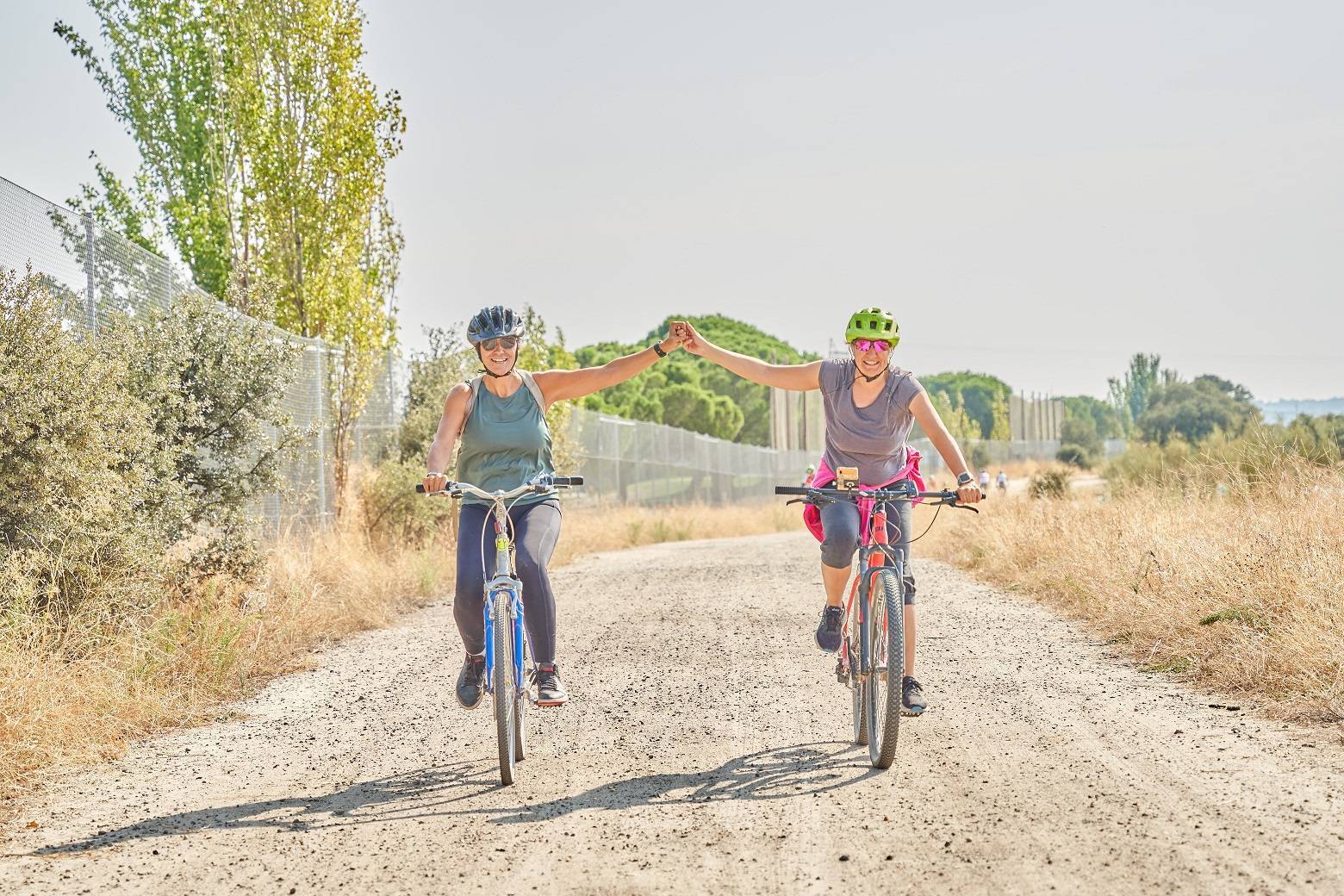 Dos mujeres en bicicleta y cogidas de la mano en el paseo rural.